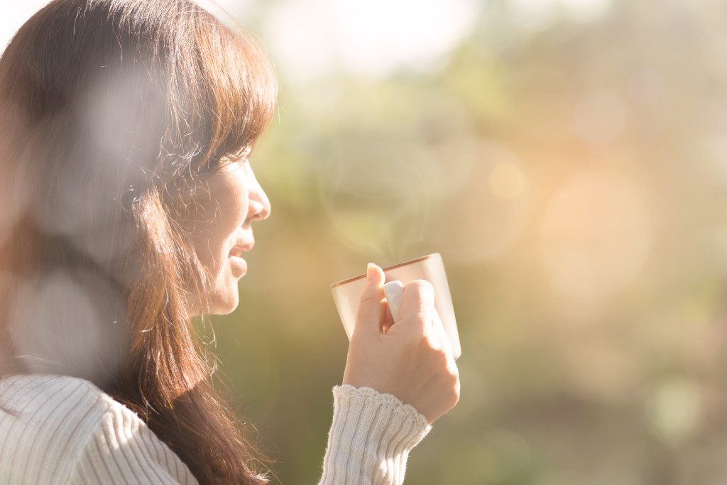 Woman feeling joyful with hand holding coffee cup at sunset on the mountain, holiday lifestyle.