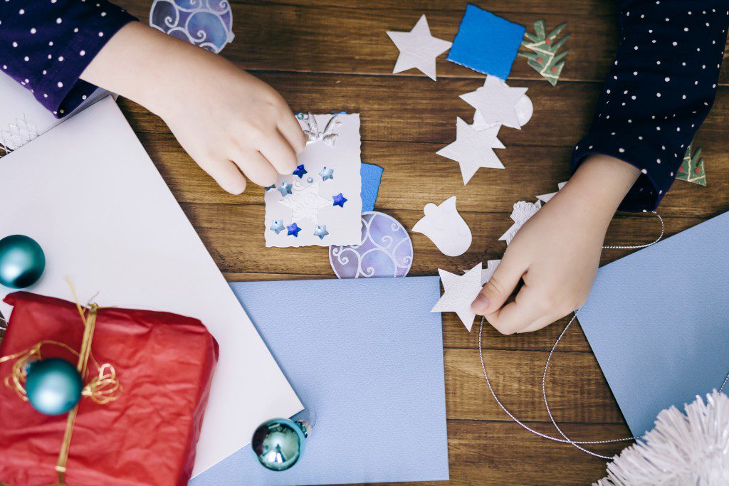 Little girl making Christmas cards on wooden background