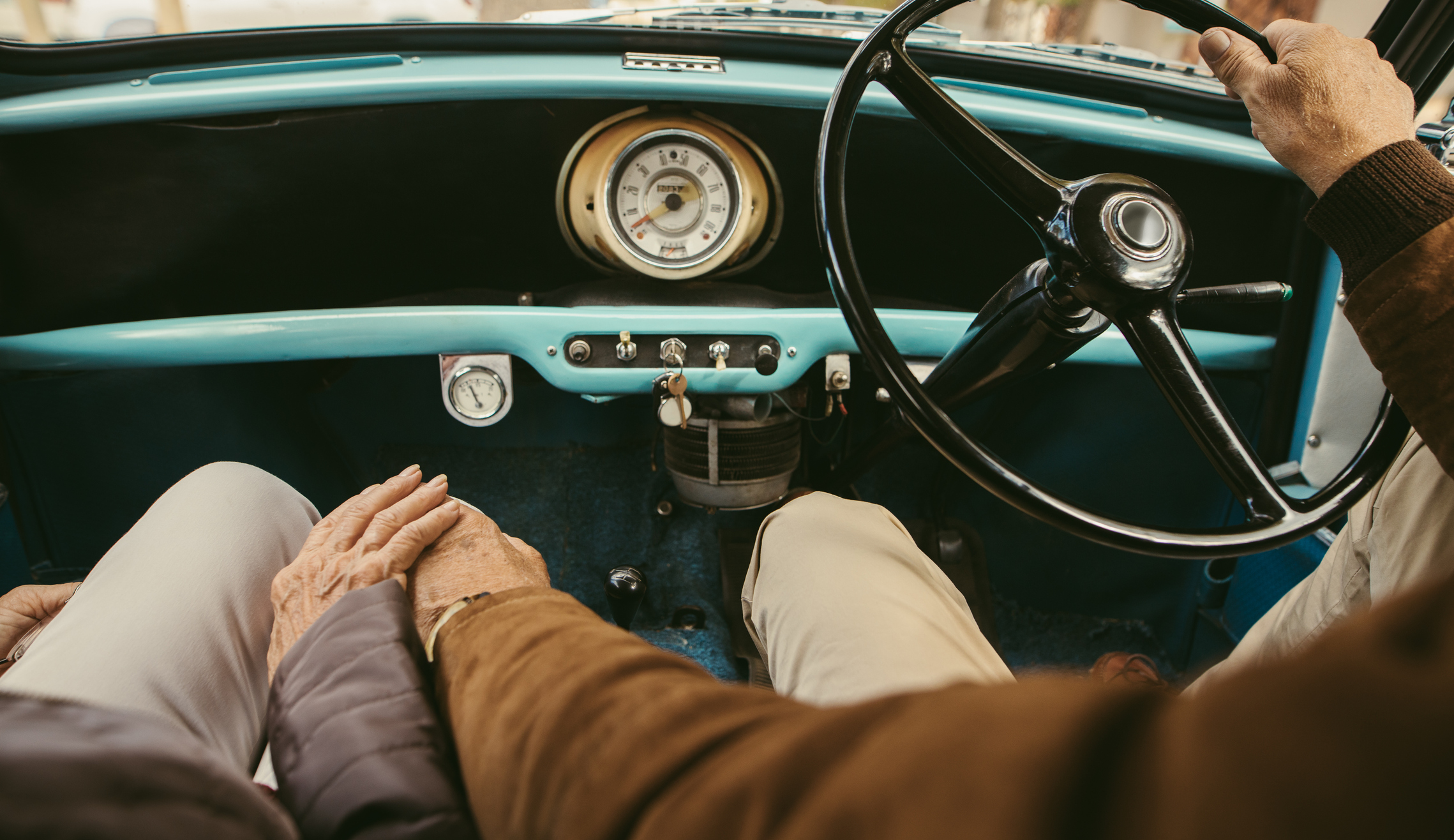 Close up of a senior couple holding hands while driving a car. Old man driving the car with woman sitting on passenger seat holding his hand.
